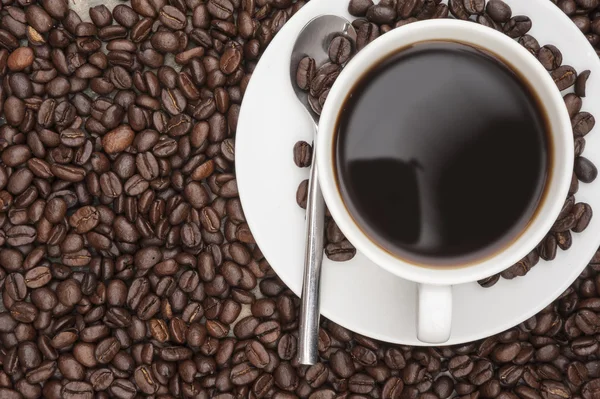 Steaming hot cup of coffee surrounded by dark coffee beans with — Stock Photo, Image