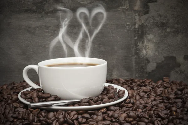 Café chaud avec de la fumée en forme de coeur, entouré de grains de café i — Photo