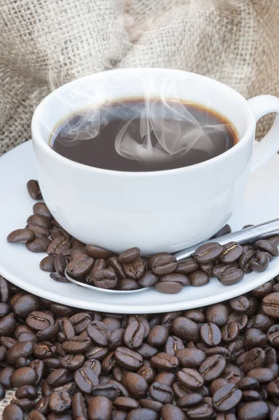 Närbild på kaffe kopp och fat omgiven av bönor på hessian — Stockfoto