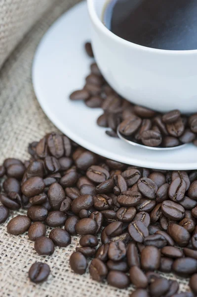 Close up of coffe cup and saucer surrounded by beans on hessian — Stock Photo, Image