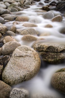 Stream flows over water worn round rocks clipart
