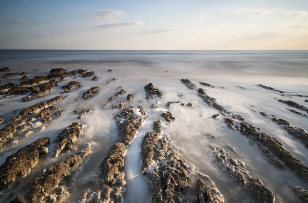 長時間露光日没時の岩が多い海岸線を風景します。 — ストック写真