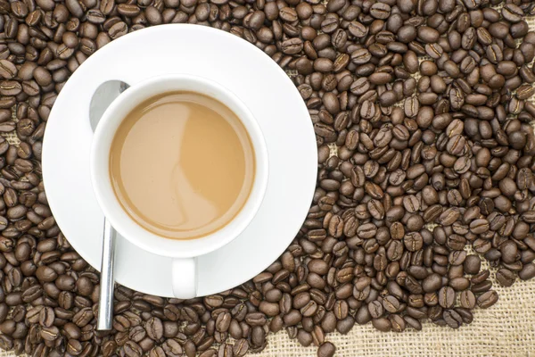 Kopp kaffe och kaffebönor på hessianen bakgrund — Stockfoto