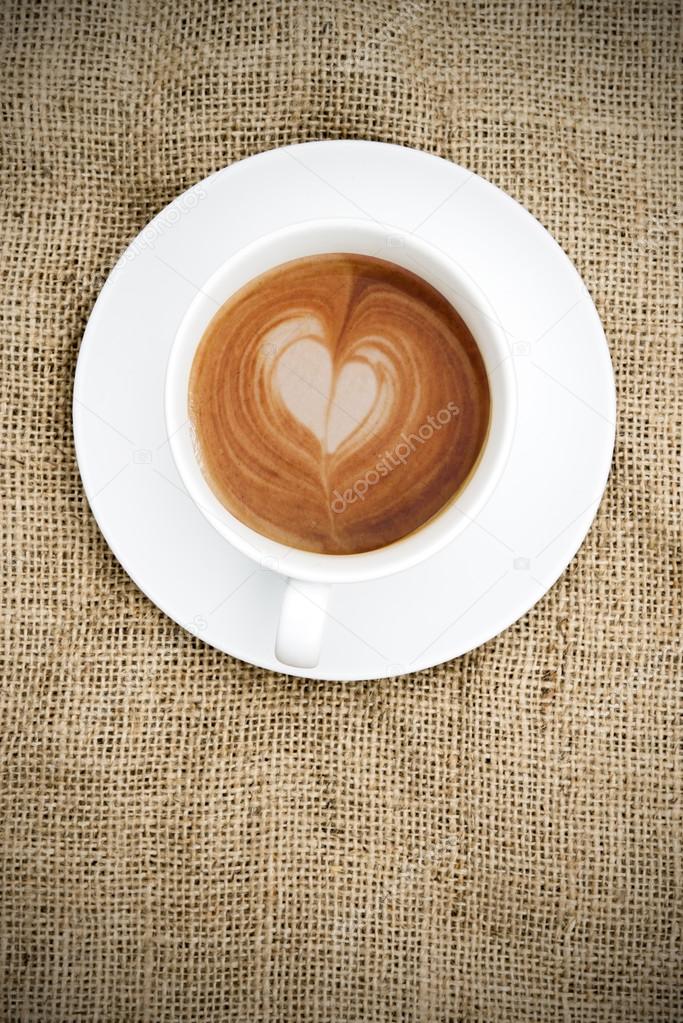 Cup of coffee with heart shape in foam on hessian background