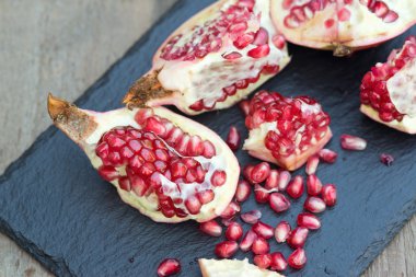 Fresh open pomegranate with seeds out on slate base and wooden b clipart