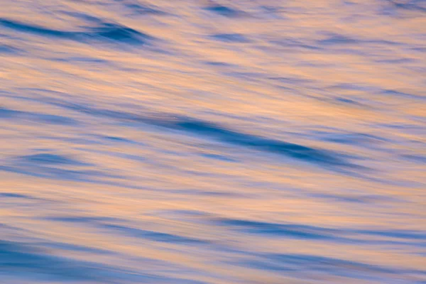 Imagem de fundo das ondas do oceano borrão com cores do nascer do sol refletem — Fotografia de Stock