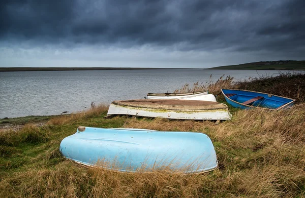 Old decayed rowing boats on shore of lake with stormy sky overhe