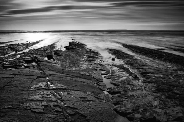 美丽的黑色和白色风景的多岩石的海岸，在日落时 — 图库照片