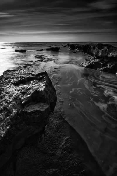 Beautiful black and white landscape of rocky shore at sunset — Stock Photo, Image