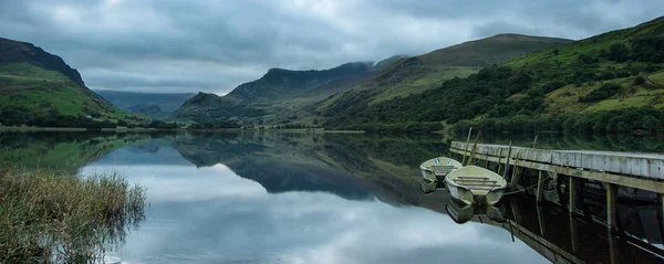 Panorama paisagem remo barcos no lago com molhe contra monte — Fotografia de Stock