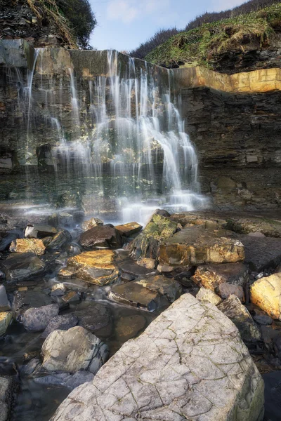 Beautiful landscape image waterfall flowing into rocks on beach