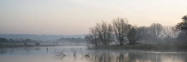 Panorama paesaggio del lago nella nebbia con bagliore di sole all'alba — Foto Stock