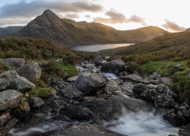 Snowdonia Ulusal Parkı 'ndaki Llyn Ogwen ve Tryfan' ın nehir ve kayalıklarla dolu destansı sonbahar günbatımı manzarası.