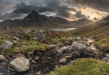 Snowdonia Ulusal Parkı 'ndaki Llyn Ogwen ve Tryfan' ın nehir ve kayalıklarla dolu destansı sonbahar günbatımı manzarası.