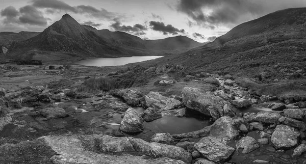 Llyn OgwenとTryfan Snowdonia国立公園の黒と白の壮大な秋の夕日の風景画像ストリームと前景色の岩 — ストック写真