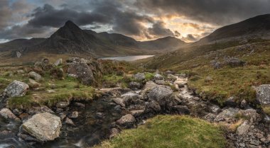 Snowdonia Ulusal Parkı 'ndaki Llyn Ogwen ve Tryfan' ın nehir ve kayalıklarla dolu destansı sonbahar günbatımı manzarası.