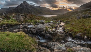 Snowdonia Ulusal Parkı 'ndaki Llyn Ogwen ve Tryfan' ın nehir ve kayalıklarla dolu destansı sonbahar günbatımı manzarası.