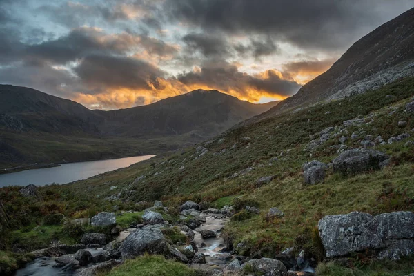 Snowdonia Ulusal Parkı 'ndaki Llyn Ogwen ve Tryfan' ın nehir ve kayalıklarla dolu destansı sonbahar günbatımı manzarası.