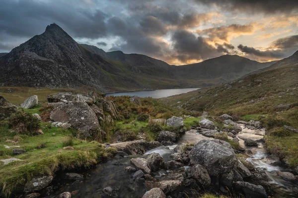Snowdonia Ulusal Parkı 'ndaki Llyn Ogwen ve Tryfan' ın nehir ve kayalıklarla dolu destansı sonbahar günbatımı manzarası.