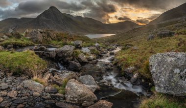 Snowdonia Ulusal Parkı 'ndaki Llyn Ogwen ve Tryfan' ın nehir ve kayalıklarla dolu destansı sonbahar günbatımı manzarası.