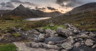 Snowdonia Ulusal Parkı 'ndaki Llyn Ogwen ve Tryfan' ın nehir ve kayalıklarla dolu destansı sonbahar günbatımı manzarası.