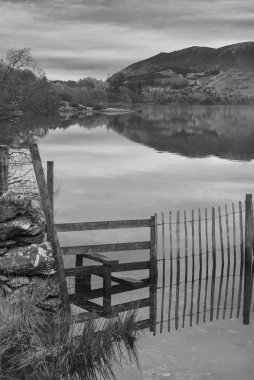 Distict Gölü 'ndeki Manesty Park' tan güneşli Skiddaw Sıradağları 'na doğru Derwentwater yüzeyi boyunca ilerleyen mit' e bakan siyah beyaz sonbahar gündoğumu manzarası