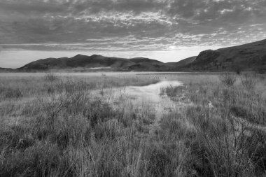Distict Gölü 'ndeki Manesty Park' tan güneşli Skiddaw Sıradağları 'na doğru Derwentwater yüzeyi boyunca ilerleyen mit' e bakan siyah beyaz sonbahar gündoğumu manzarası