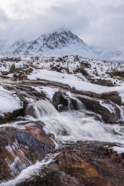 Önplanda Etive Nehri 'nin güzel kış manzarası. Arkaplanda ikonik kar örtülü Stob Dearg Buachaille Etive Mor dağı var.