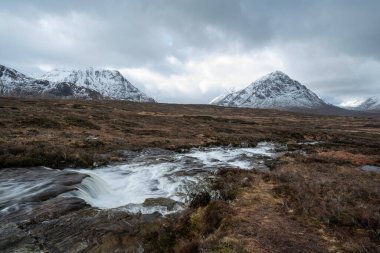 Önplanda Etive Nehri 'nin güzel kış manzarası. Arkaplanda ikonik kar örtülü Stob Dearg Buachaille Etive Mor dağı var.