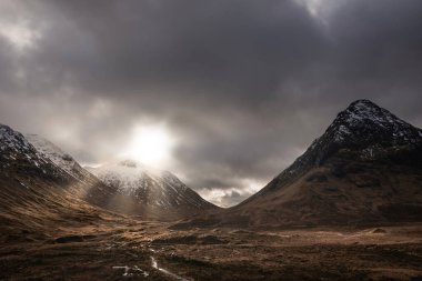 İskoçya 'daki Etive Mor' un destansı kış manzarası. Dağların zirveleri arasından güneş ışınları akıyor.
