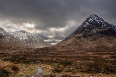İskoçya 'daki Etive Mor' un destansı kış manzarası. Dağların zirveleri arasından güneş ışınları akıyor.