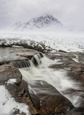 Önplanda Etive Nehri 'nin güzel kış manzarası. Arkaplanda ikonik kar örtülü Stob Dearg Buachaille Etive Mor dağı var.