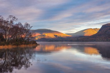 Distict Gölü 'ndeki Manesty Parkı' ndan Derwentwater yüzeyi boyunca ilerleyen güz güneşli Skiddaw Sıradağları 'na bakan destansı gündoğumu manzarası.