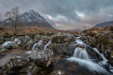 Enfes kış günbatımı manzarası Stob Dearg Buachaille Etive Mor ikonik zirvesi İskoç Dağları 'nda ünlü nehir şelaleleri ön planda.