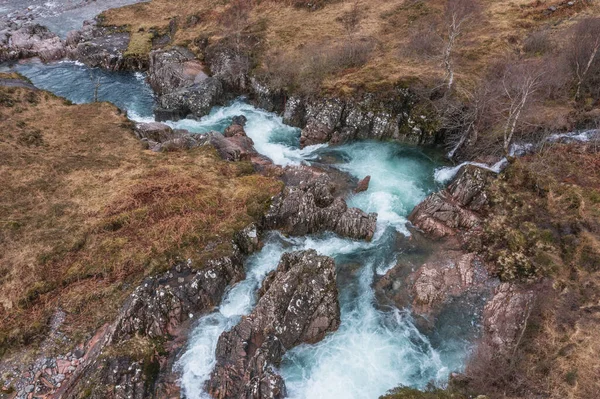 Beautiful aerial drone landscape image of vibrant River Coe flowing beneath snowcapped mountains in Scottish Highlands