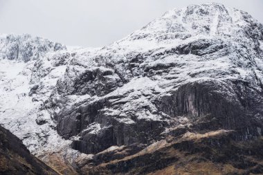 Glencoe İskoç dağlarında kar tepeli üç kız kardeşin dramatik gökyüzü eşliğinde destansı kış manzarası