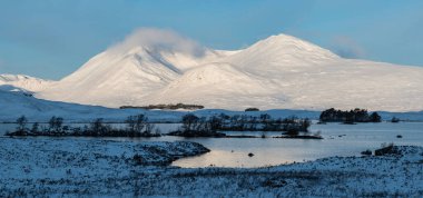 Beautiful landscape image in Winter looking across Lochan Na h-Achlaise towards mountain ranges in Scottish Highlands
