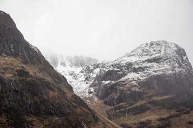 Glencoe İskoç dağlarında kar tepeli üç kız kardeşin dramatik gökyüzü eşliğinde destansı kış manzarası