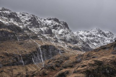 Glencoe İskoç dağlarında kar tepeli üç kız kardeşin dramatik gökyüzü eşliğinde destansı kış manzarası