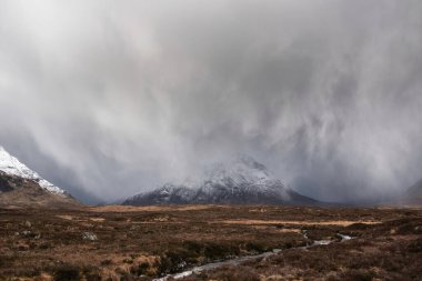 Winter landscape image of Stob Dearg Buachaille Etive Mor viewed from Rannoch Moor with snowcapped peak with heavy rain shower passing through the valley