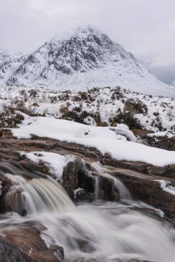 Önplanda Etive Nehri 'nin güzel kış manzarası. Arkaplanda ikonik kar örtülü Stob Dearg Buachaille Etive Mor dağı var.