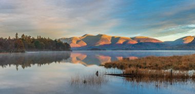 Distict Gölü 'ndeki Manesty Parkı' ndan Derwentwater yüzeyi boyunca ilerleyen güz güneşli Skiddaw Sıradağları 'na bakan destansı gündoğumu manzarası.