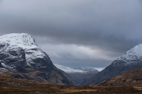 Glencoe İskoç dağlarında kar tepeli üç kız kardeşin dramatik gökyüzü eşliğinde destansı kış manzarası