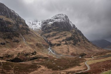 Glencoe İskoç dağlarında kar tepeli üç kız kardeşin dramatik gökyüzü eşliğinde destansı kış manzarası