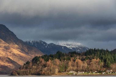 Güzel kış manzarası, Leven Gölü boyunca dramatik gökyüzü ile uzaktaki karlı dağlara doğru.