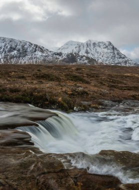 Önplanda Etive Nehri 'nin güzel kış manzarası. Arkaplanda ikonik kar örtülü Stob Dearg Buachaille Etive Mor dağı var.