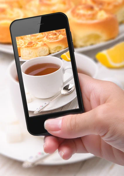 Руки делают фото булочки с сыром со смартфоном — стоковое фото