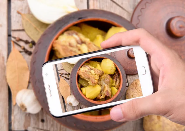 Mãos tirando fotos de batatas com carne com smartphone — Fotografia de Stock