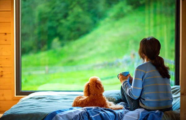 女性はベッドの上に座ってお茶を飲んで窓の外を見る山 — ストック写真