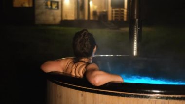 Genç bir kadın açık hava banyosunda ve dağları görüyor..